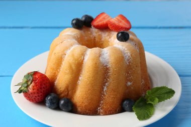 Açık mavi ahşap masada pudra şekerli ve dutlu Lezzetli kek, yakın plan.