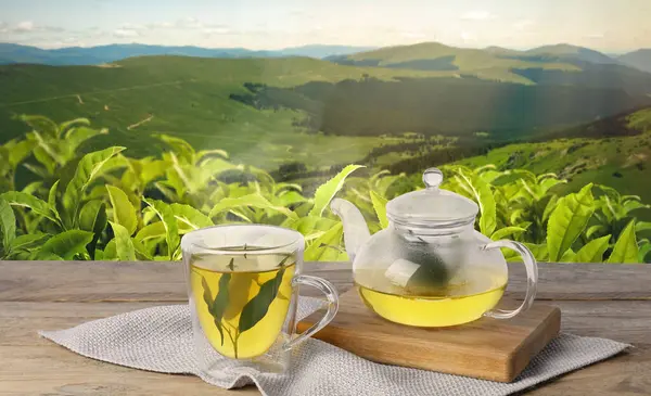 Yeşil çay fincanda, çaydanlık da ahşap masada, dağlardaki çay tarlasına karşı. Pankart tasarımı