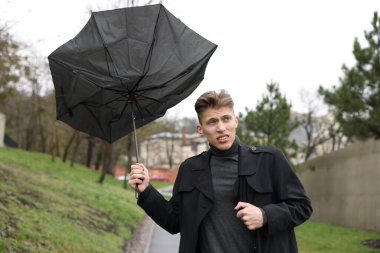 Kırık şemsiyeli bir adam açık havada yağmur altında rüzgarla savaşıyor.