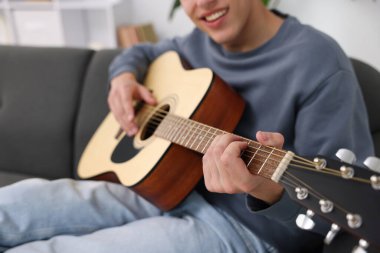 Genç adam kanepede gitar çalıyor, yakın plan.