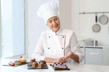 Gülümseyen pasta şefi mutfaktaki tatlılarla masada.