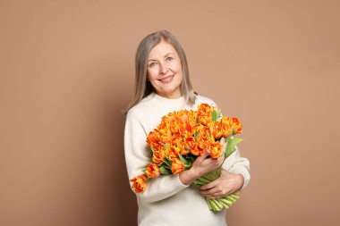 Bej arka planda bir buket lale ile gülümseyen kadın.