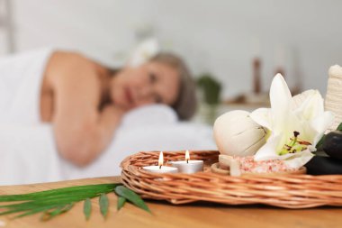 Masaj koltuğunda dinlenen yaşlı bir kadın, seçici bir odak noktası. Masada farklı spa ürünleri ve zambak çiçeği var.