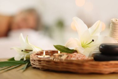 Masaj koltuğunda dinlenen yaşlı bir kadın, seçici bir odak noktası. Masada farklı spa ürünleri ve zambak çiçekleri