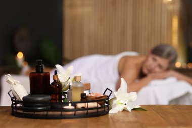 Üst düzey kadın masaj koltuğunda dinleniyor, farklı spa ürünlerine ve zambak çiçeklerine odaklanıyor.