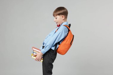 Sırt çantası ve açık gri arka plan kitapları olan sevimli bir okul çocuğu.