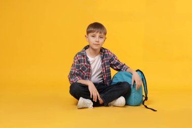 Turuncu arka planda sırt çantası olan tatlı bir okul çocuğu.
