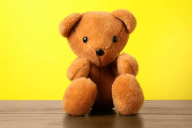 Tahta masada sarı arka planda sevimli bir oyuncak ayı.