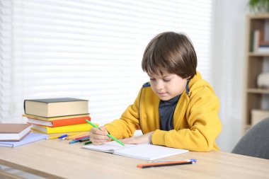 Evde, masada ödev yapan sevimli küçük çocuk.