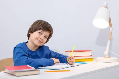 İçeride masa başında ödev yapan sevimli küçük çocuk.