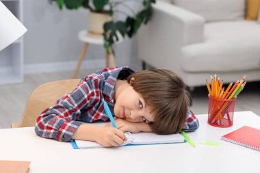 Evde, masada ödev yapan sevimli küçük çocuk.