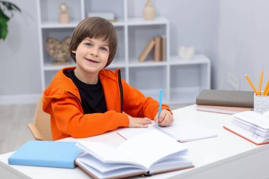 İçeride masa başında ödev yapan sevimli küçük çocuk.