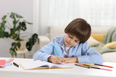 İçeride masa başında ödev yapan sevimli küçük çocuk.