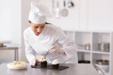 Şekerci mutfakta bir parça çikolatayla kek dekore ediyor.