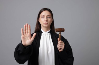 Elinde tokmak olan yargıç gri arkaplanda dur işareti yapıyor.