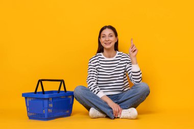 Sarı arka planda, elinde alışveriş sepeti olan gülümseyen kadın.