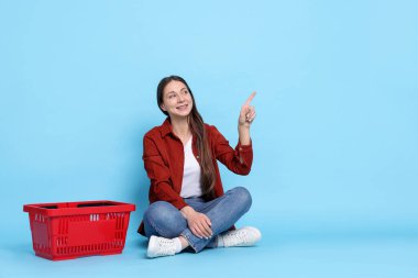 Gülümseyen kadın bir şeyi işaret ediyor ve açık mavi arka planda alışveriş sepeti. Metin için boşluk