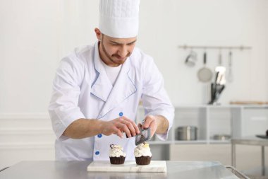 Şekerci çikolatayı mutfaktaki masada kekin üzerine rendeliyor, mesaj için yer var.