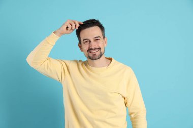 Yakışıklı adam saçlarını açık mavi arka planda tarak ile tarıyor.