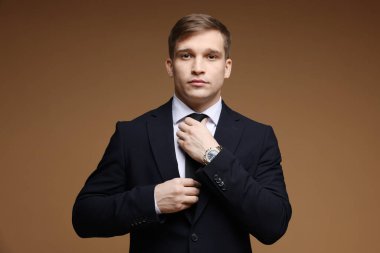 Kahverengi arka planda şık saati olan klasik takım elbiseli bir adam.