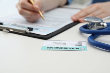 Beyaz masada kalem poliçesi dolduran doktor, sağlık sigortası kartına odaklan.