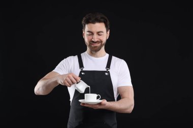Gülümseyen barista siyah arka planda kahve yapıyor.