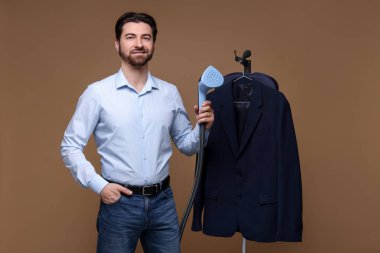 Kahverengi arka planda vapuru ve ceketi olan adam.