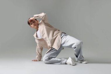 Açık gri arka planda dans eden şık elbiseli bir çocuk.