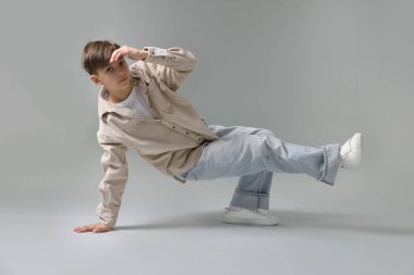 Açık gri arka planda dans eden şık elbiseli bir çocuk.