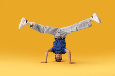 Şık giyinmiş çocuk turuncu arka planda dans ediyor.