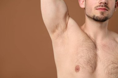 Genç adam kahverengi arka planda kıllı koltuk altlarını gösteriyor, yakın plan. Epilasyon işlemi