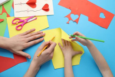 Anne ve kızı açık mavi masada el yapımı bir proje yapıyor.