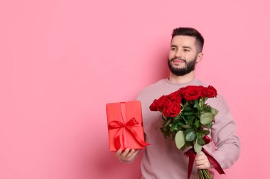 Kırmızı gül buketi ve pembe arka planda hediye kutusu olan bir adam.