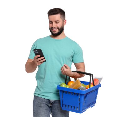 Beyaz arka planda akıllı telefon kullanan bir sepet dolusu ürünü olan adam.