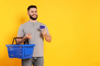 Boş alışveriş sepeti ve turuncu arka planda kredi kartı olan adam, mesaj için boşluk