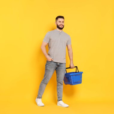 Turuncu arka planda boş alışveriş sepeti olan adam.