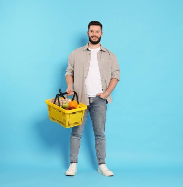 Açık mavi arka planda ürünlerle dolu alışveriş sepeti olan bir adam.