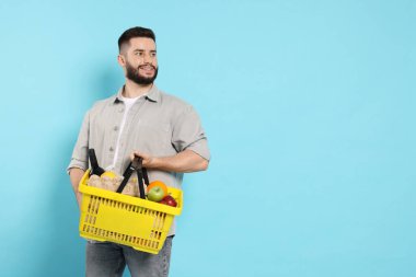 Açık mavi arka planda ürünlerle dolu alışveriş sepeti olan adam, metin için yer