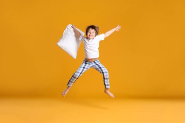 Turuncu arka planda yastıkla zıplayan tatlı çocuk.