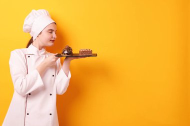 Üniformalı şekerlemeci turuncu arka planda lezzetli çikolatalı tatlılar tutuyor, mesaj için yer var.