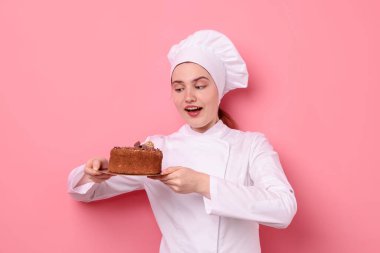 Üniformalı pastacı pembe arka planda lezzetli çikolatalı pasta tutuyor.