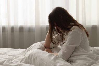 Evdeki yatakta oturan üzgün genç kadın.