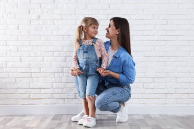 Güzel anne ve küçük kızı beyaz tuğla duvarın yanında