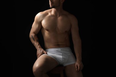 Siyah arka planda beyaz iç çamaşırlı genç adam, yakın plan.