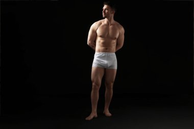 Siyah arka planda beyaz iç çamaşırlı genç bir adam.