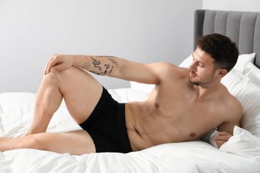 Siyah iç çamaşırlı genç adam yatağın içinde.