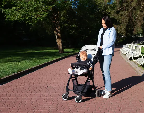 Anne bebeğiyle parkta bebek arabasında yürüyor.