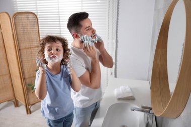 Banyoda yüzlerinde tıraş köpüğü olan mutlu baba ve oğlu.