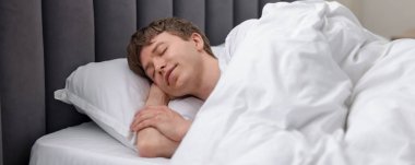 Genç adam yatağında uyuyor.