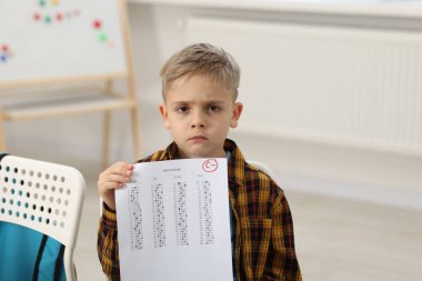 Okul derecesi. Kapalı alanda C harfi ve eksi sembolle cevap kağıdını tutan üzgün çocuk.